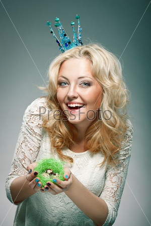 emotional portrait of woman wearing  blue princess crown and holding nest with quail eggs