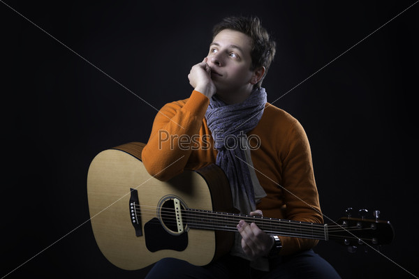 Dreaming man on background posing with acoustic guitar.