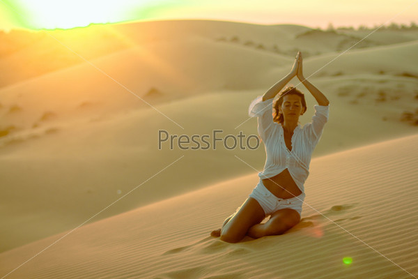 Beautiful woman meditating in desert, stock photo