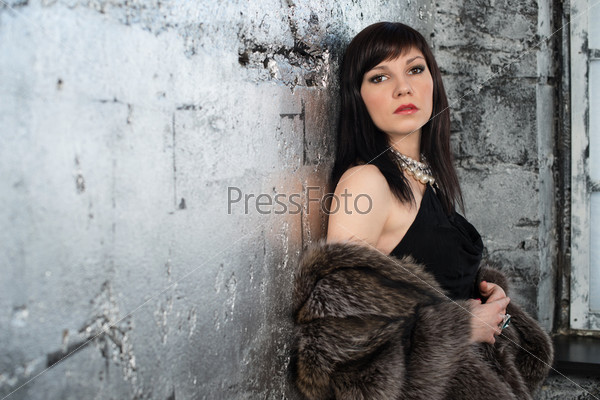 Elegant dark-haired caucasian woman wearing fur coat and jewelry, studio shot