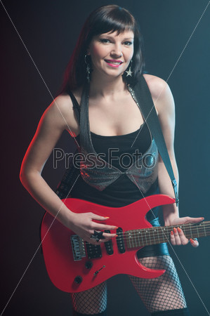 Smiling dark-haired rock lady posing with electric guitar over dark background, vertical shot