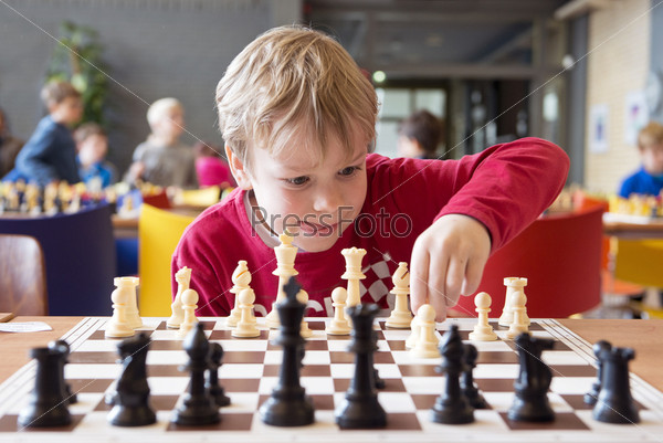 Young child making a move with a horse during a chess tournament at a school, with several other competitors in the background