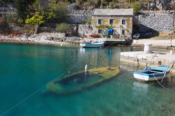 View of old stone house with a wooden boat sunk in little bay