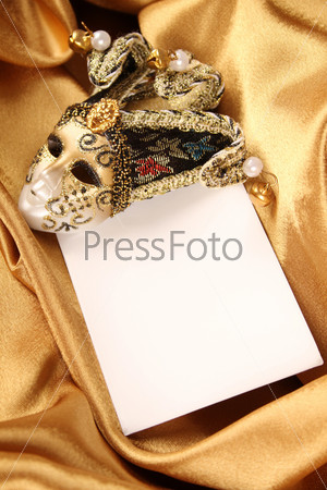 Carnival mask lying on a yellow silk and a sheet of white paper