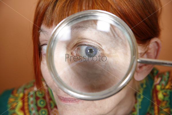 Red haired woman with blue eye peering through a magnifying glass