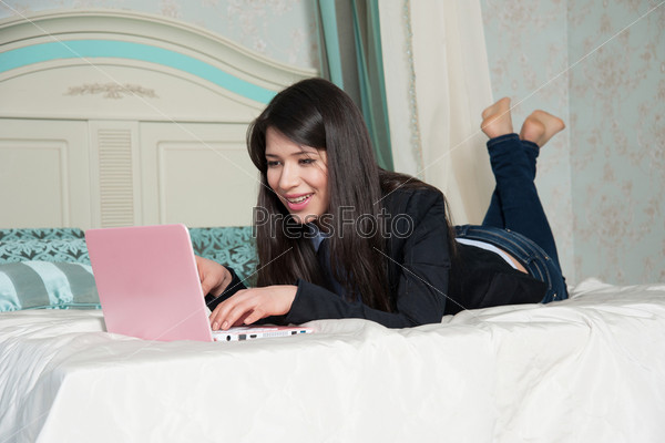 Женщина лежит на кровати с ноутбуком