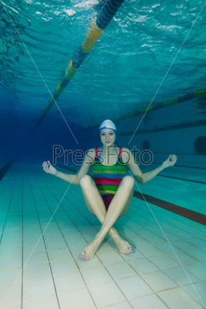 Underwater yoga - girl sitting on the pool floor and meditating