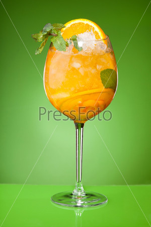 Refreshing summer orange drink with ice and mint on green background