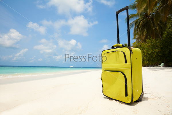 Suitcase on the beach with white sand, sunny sky and palms representing vacation travel concepts