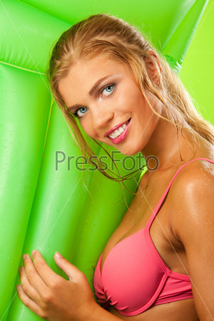 studio shot of attractive tanned girl in bikini smiling and holding green mattress