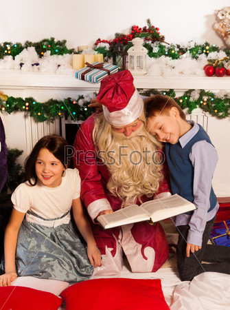 Santa Claus reading books to kids sitting by fireplace