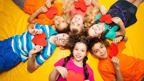 Group of happy kids laying in circle on the floor with hearts in their hands