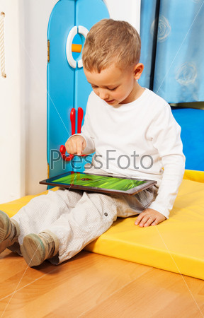 Blond five years old boy occupied with tablet computer touching screen with finger