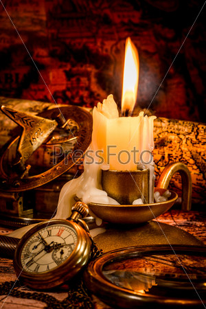 Vintage compass, pocket watch lie on an old ancient map with a lit candle, stock photo