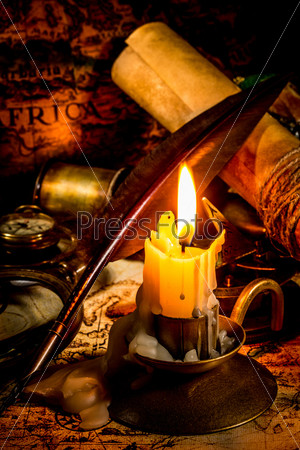 Vintage compass, magnifying glass, quill pen, spyglass lie on an old ancient map with a lit candle