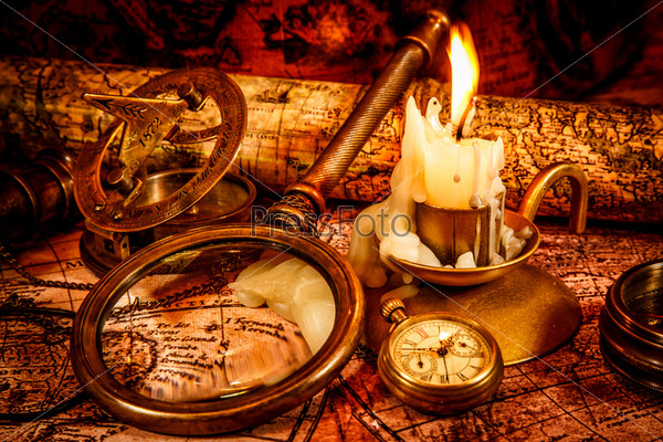 Vintage compass, magnifying glass, spyglass lie on an old ancient map with a lit candle. Vintage still life.
