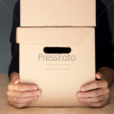 Successful Postal or delivery service concept. Man holding cardboard box with two arms on table