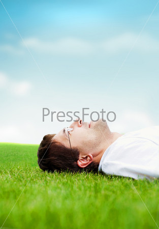 Young good looking man in white shirt lying on grass and looking at the sky