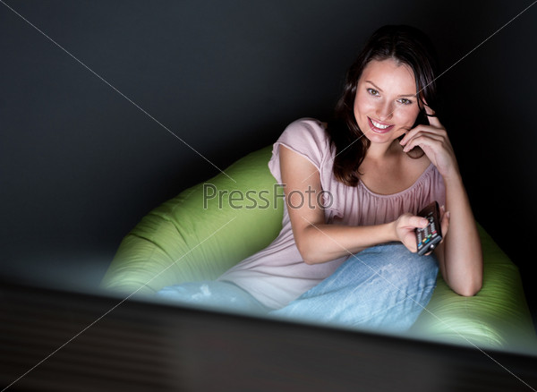 Young woman watching TV sitting on the beanbag at home