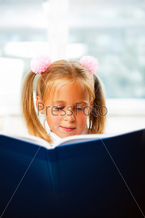 Image of smart child reading interesting book in classroom. Vertical Shot. She is involved and attentive