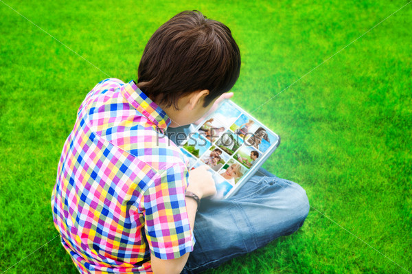 Little boy sitting on grass and using tablet computer to watch or share photo and video files