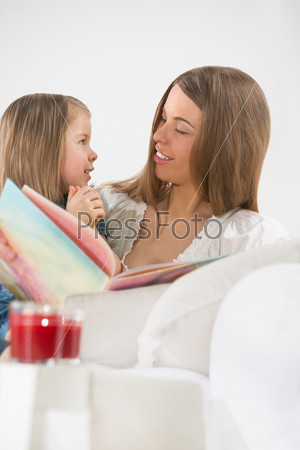 Young mother and daughter reading a book together on the sofa