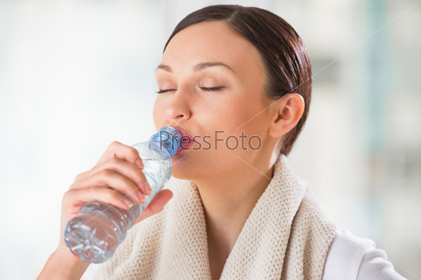 Portrait of young woman drinking water at gym after doing exercises