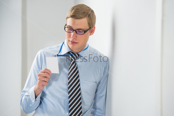 Happy smiling business man showing blank badge, while leaning on wall at office
