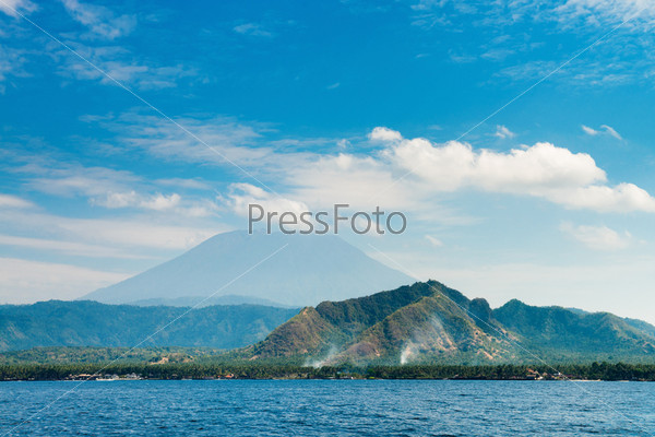Gunung Agung the highest volcano on Bali island, Indonesia with blue cloudy sky and sea on front.