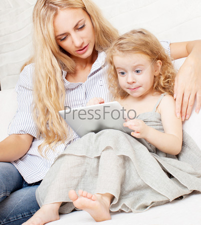 Family wiht tablet at sofa. Woman and baby with tablet computer. Mother and daughter at home on sofa
