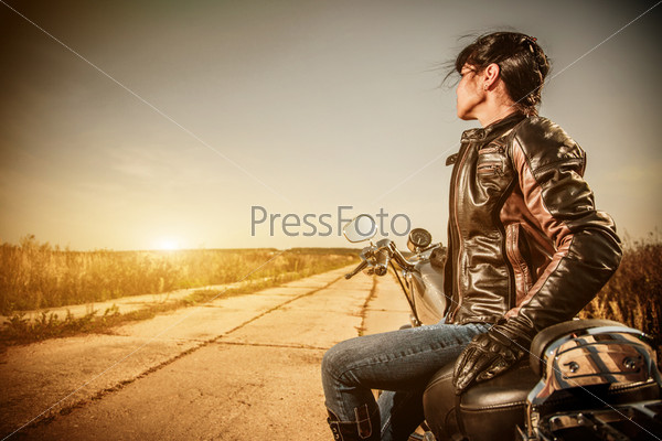 Biker Girl In A Leather Jacket On A Motorcycle Looking At The Sunset.