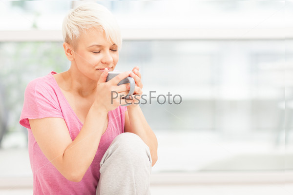 Photo of smiling woman with mug sitting on the floor while smiling