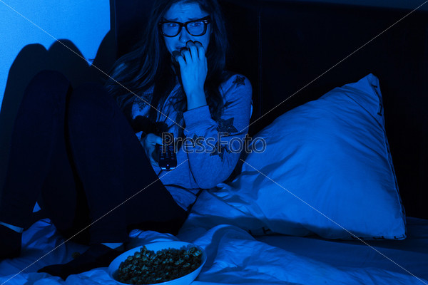 Young woman watching scary movie at home darkness