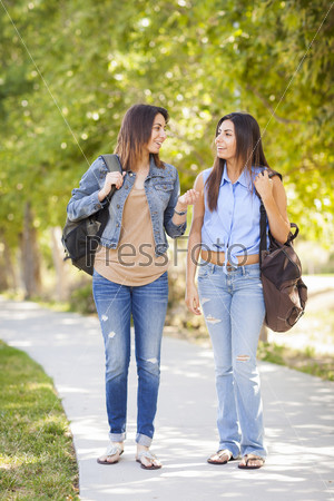 Young Adult Mixed Race Twin Sisters Walking Together Wearing Backpacks Outside.