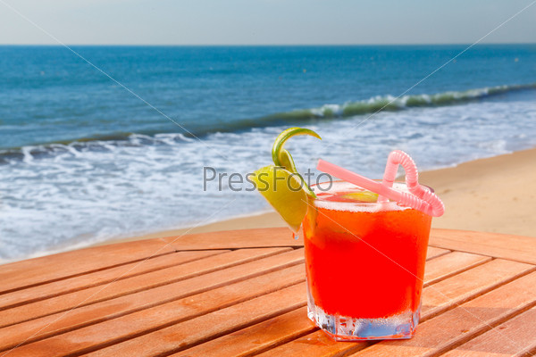 red alcohol cocktail on the wooden table with crushed ice on background blue sky and sea