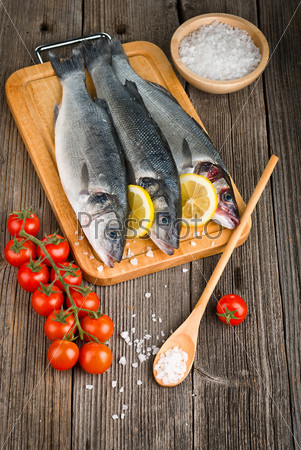 Sea Bass with salt, tomatoes and lemon, on wooden background
