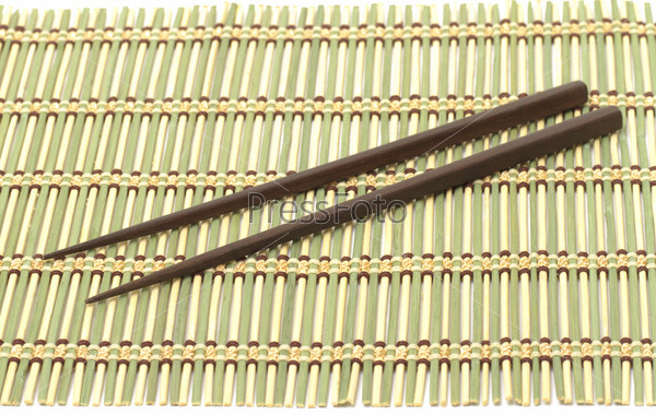 Dark wooden chopsticks on bamboo mat