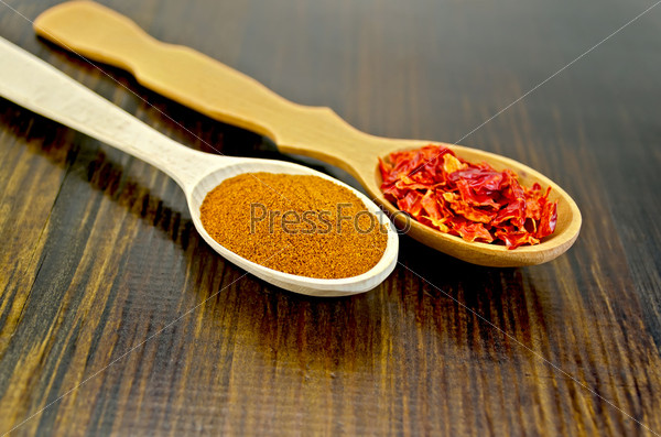 Powder and flakes of red pepper in wooden spoons on a wooden board, stock photo