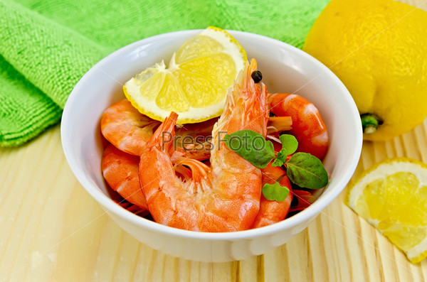 Raw shrimp in a white bowl with lemon, basil and green cloth on a wooden board