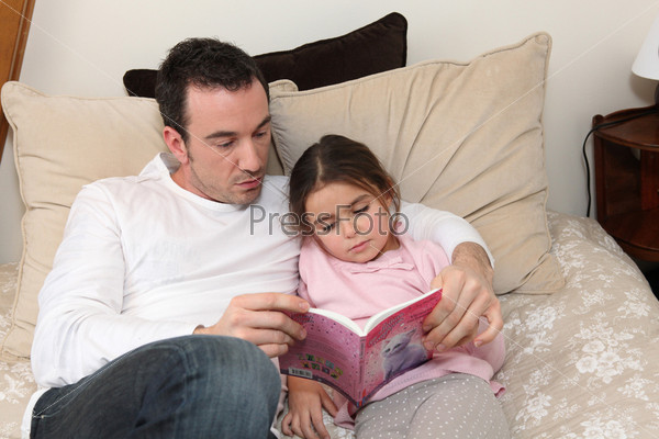 Man reading story to little girl in bed