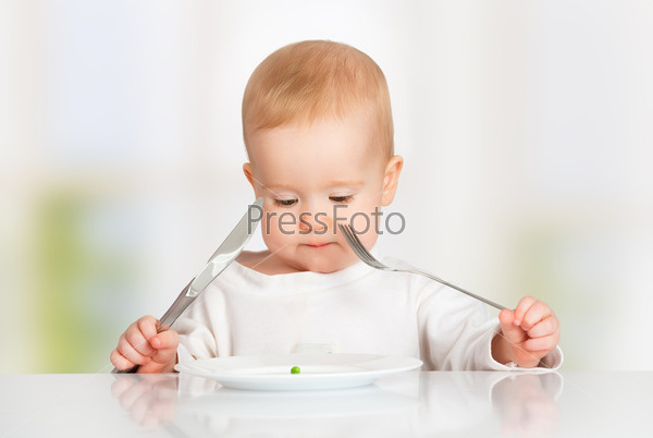 concept. funny baby with fork and knife eating, looking at the plate with one pea
