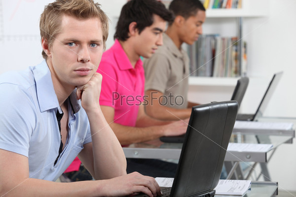 Three male students with laptops in classroom, stock photo