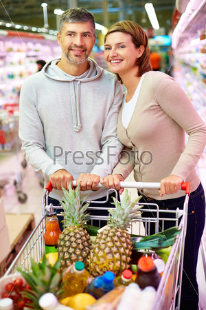 Image of happy couple with cart choosing products in supermarket