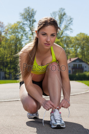 Beautiful young woman in fitness wear ties shoelaces outdoors, stock photo