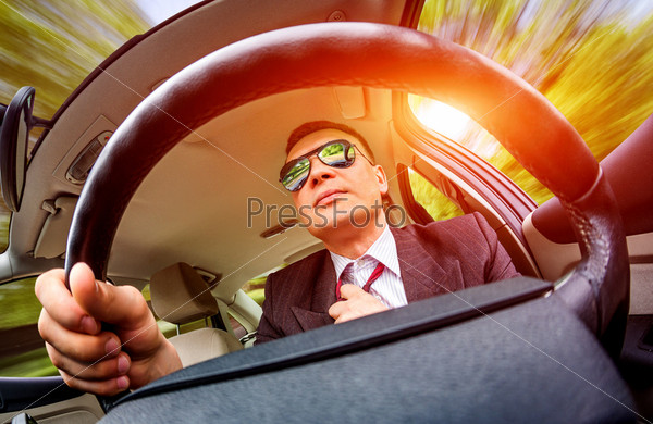 Man in a suit and sunglasses driving on a road in the car.