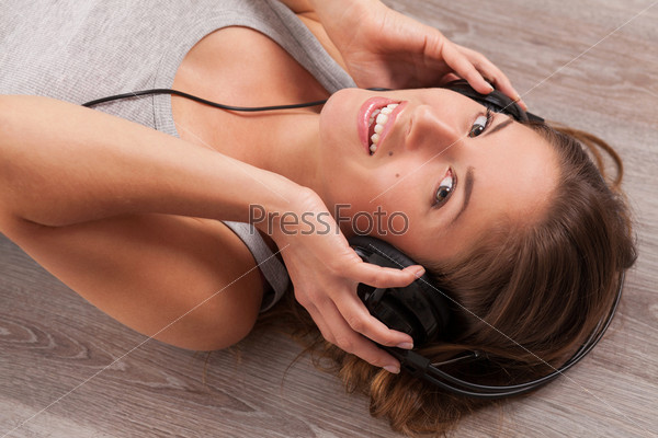 Beautiful caucasian woman listening music with headphones lying on the wooden floor, stock photo