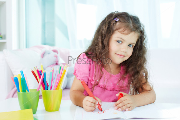 Portrait of lovely girl looking at camera while drawing with colorful pencils