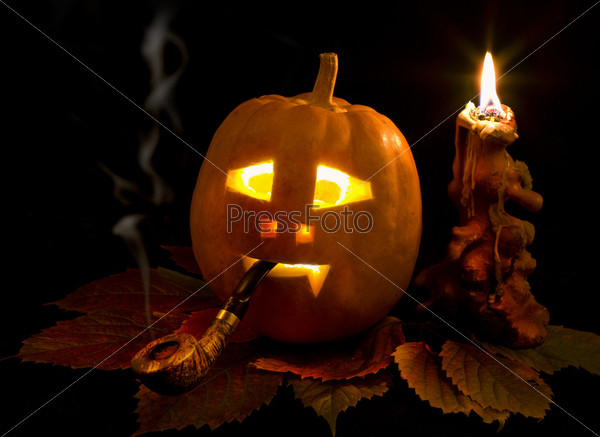Halloween pumpkin on leaves with smoke pipe and candle