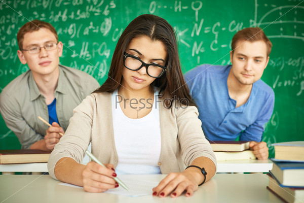 Portrait of smart student carrying out test with two guys behind looking at her paper