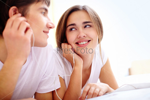 Portrait of young couple listening to music in earphones in bed